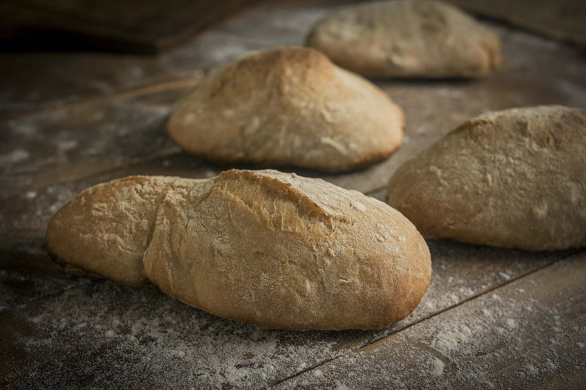 Rustic no-knead ciabatta rolls on a flour-dusted wooden surface.